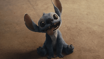 A small blue alien creature with large ears and big eyes, sitting and sticking out its tongue.