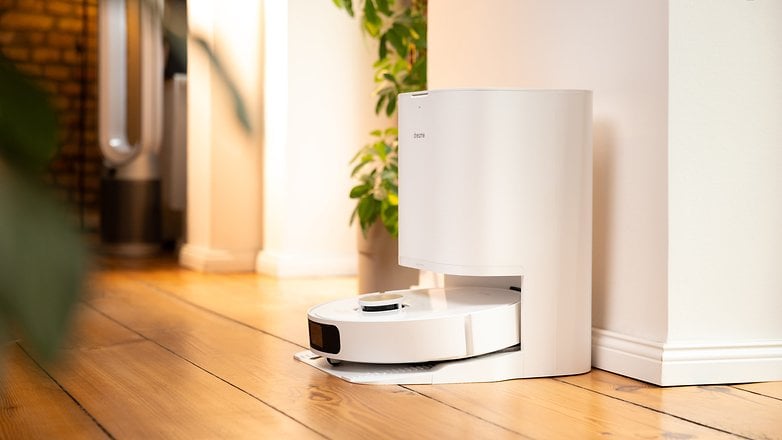 Un aspirateur robot blanc amarré à un mur avec des plantes dans un espace intérieur moderne. Un aspirateur robot blanc amarré à un mur avec des plantes dans un espace intérieur moderne.